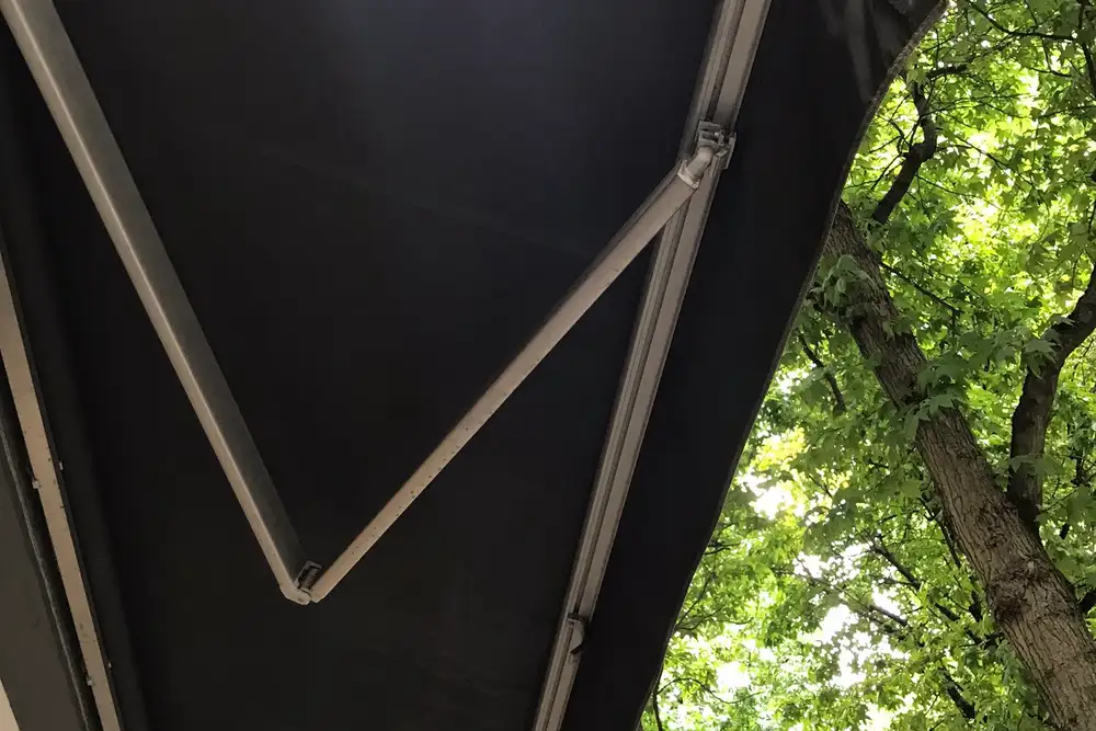 Toldo de brazos articulados extendido visto desde abajo, con la lona oscura y los brazos de aluminio abiertos