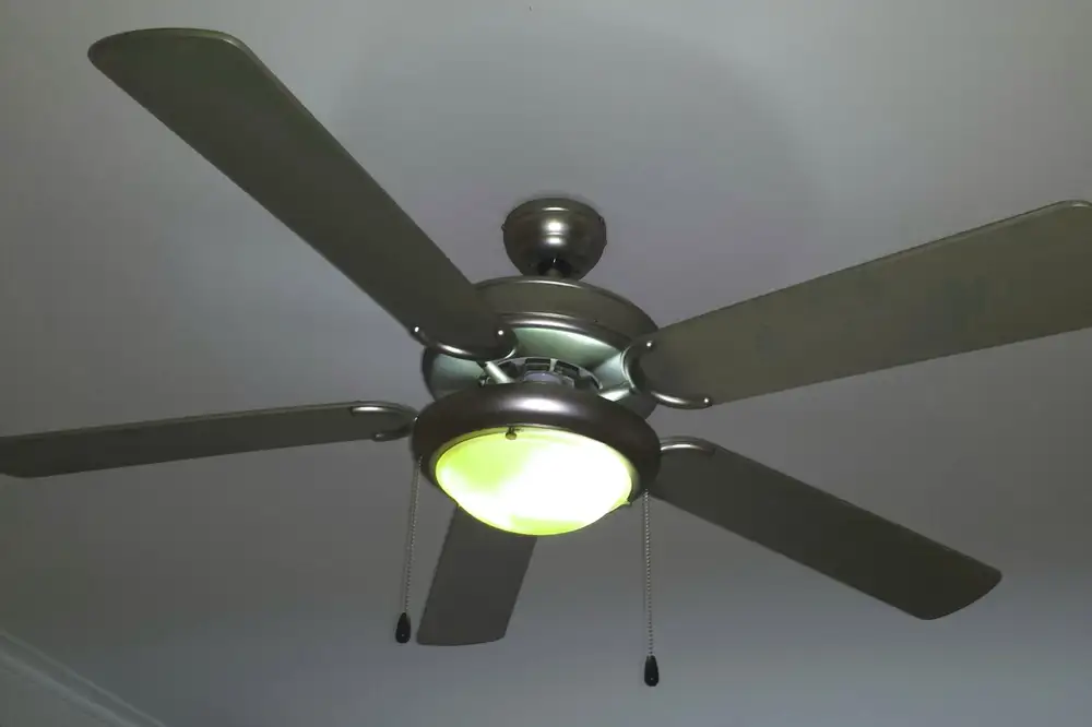 Ventilador de techo de cinco aspas con lámpara central encendida y dos cadenas de tiro colgando