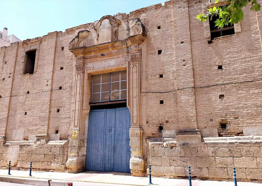 Fachada de ladrillo con portada de piedra y puerta azul del antiguo convento de los Mínimos de Alcantarilla